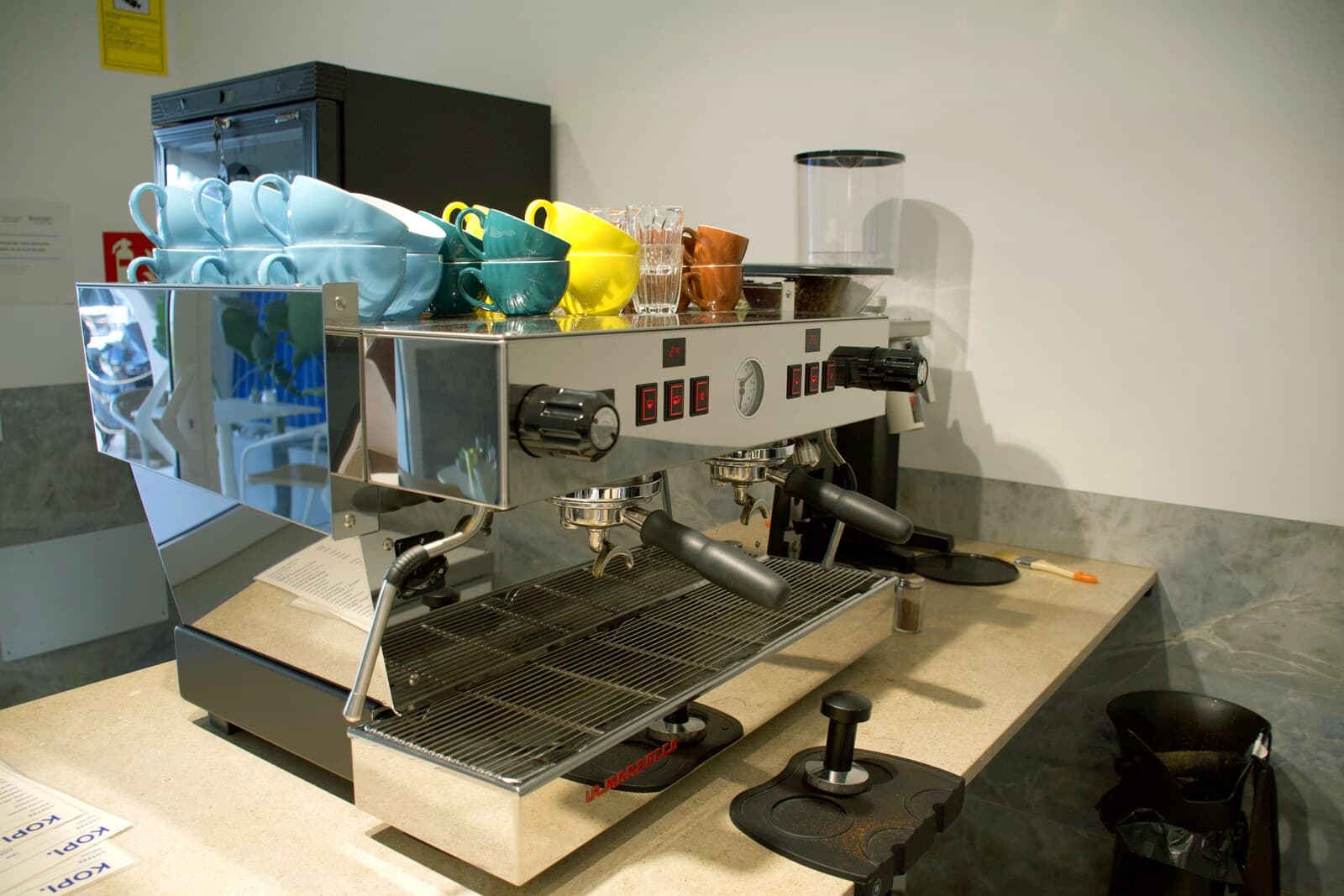 La máquina La Marzocco con las tazas de colores y el molinillo